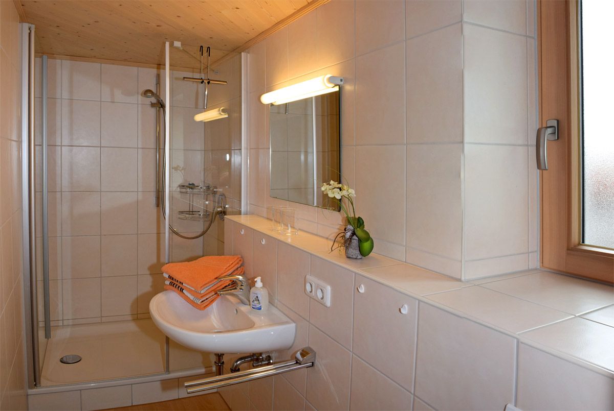 Badezimmer mit Dusche, Waschbecken, Spiegel und Tageslichtfenster